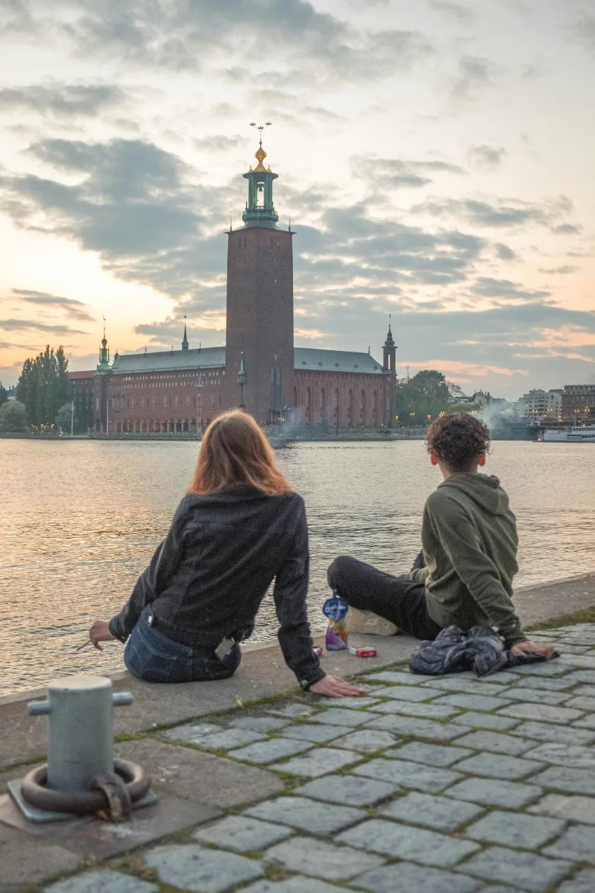 People sitting by the water looking at Stockholm City Hall during sunset